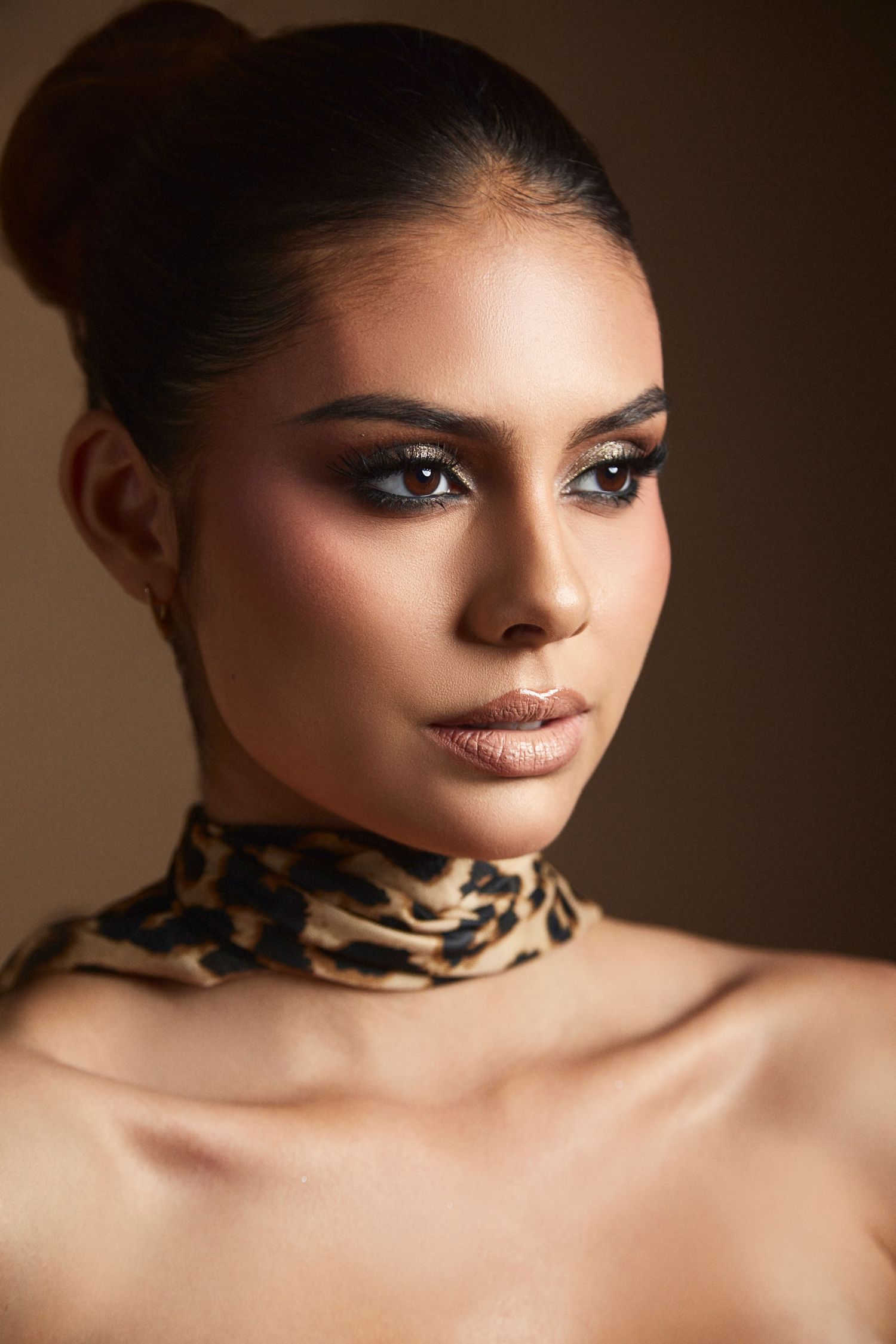 Close-up beauty portrait with dramatic lighting showcasing glamorous makeup and animal print choker.