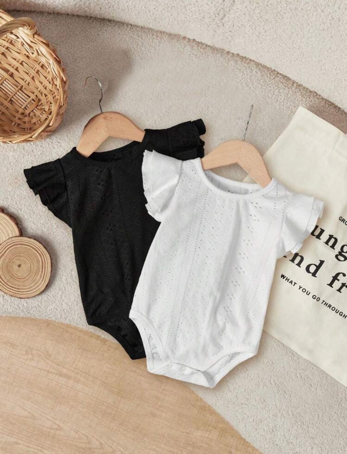 Black and white flutter sleeve baby bodysuits laid flat on beige surface with natural decor.