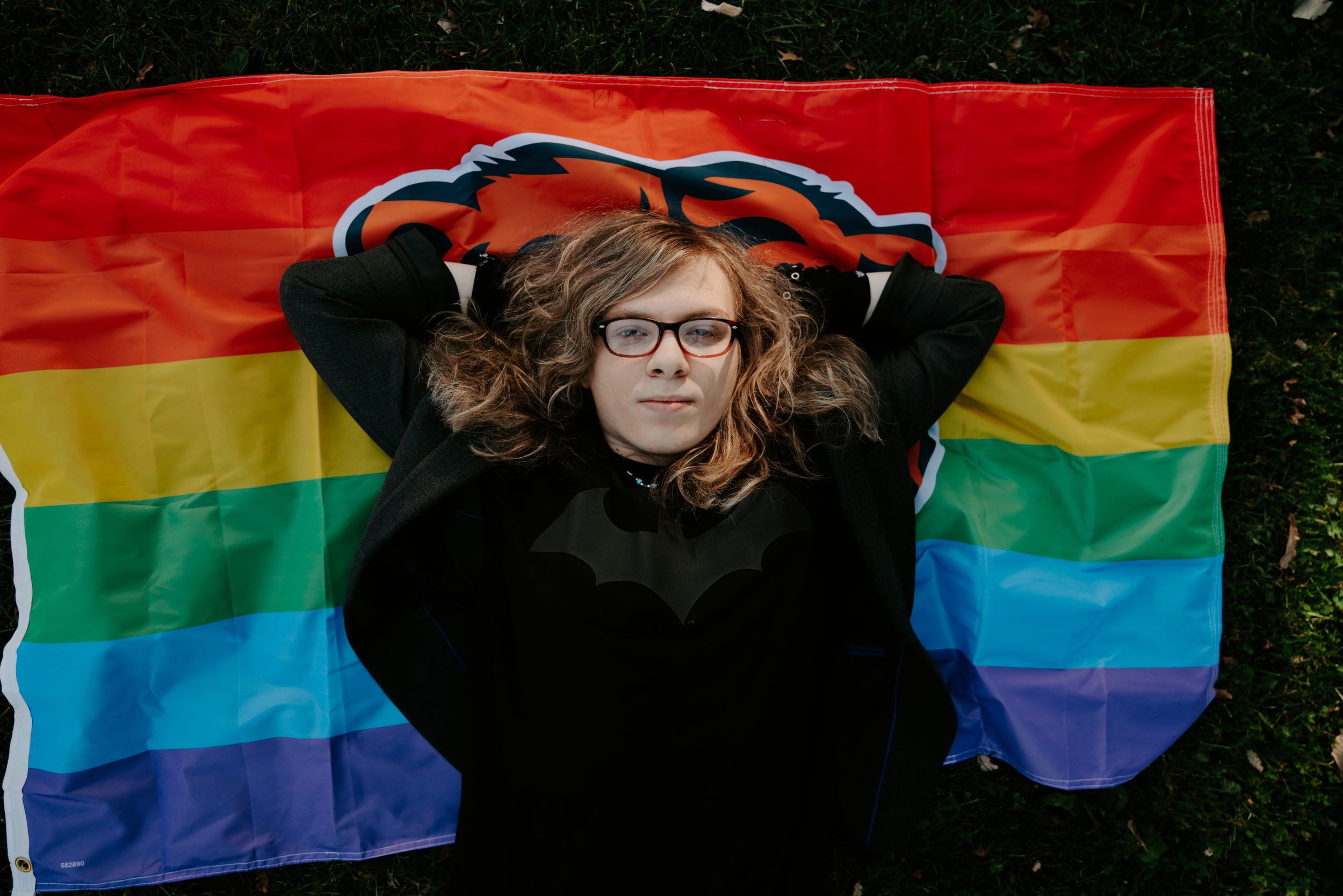 Someone poses with a rainbow pride flag against a dark background.