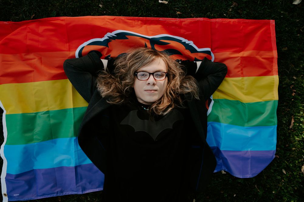 Someone poses with a rainbow pride flag against a dark background.