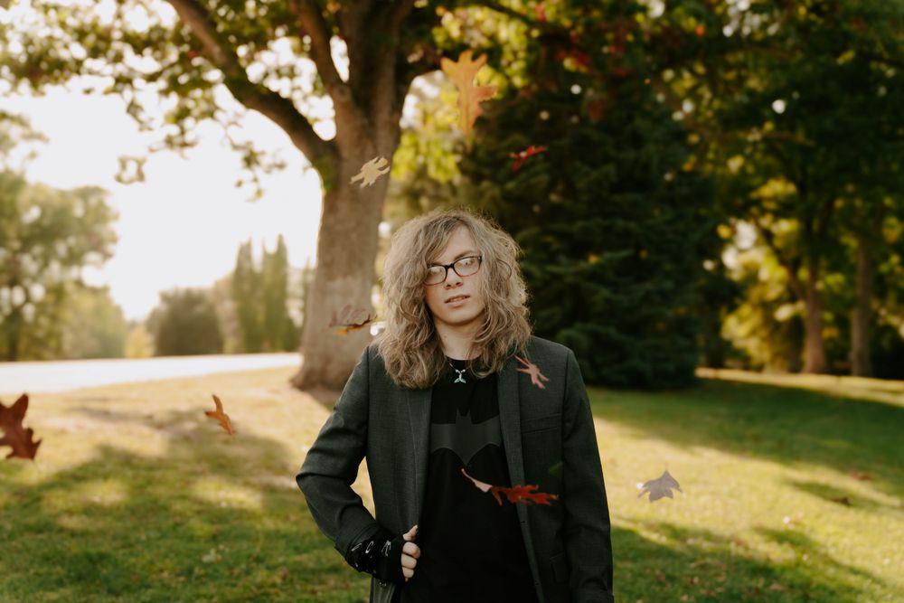 Someone poses outdoors on a grassy hillside during golden hour.