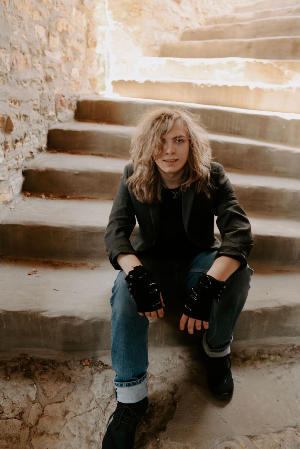 Person in black attire sitting on stone steps in a moody sepia-toned portrait.