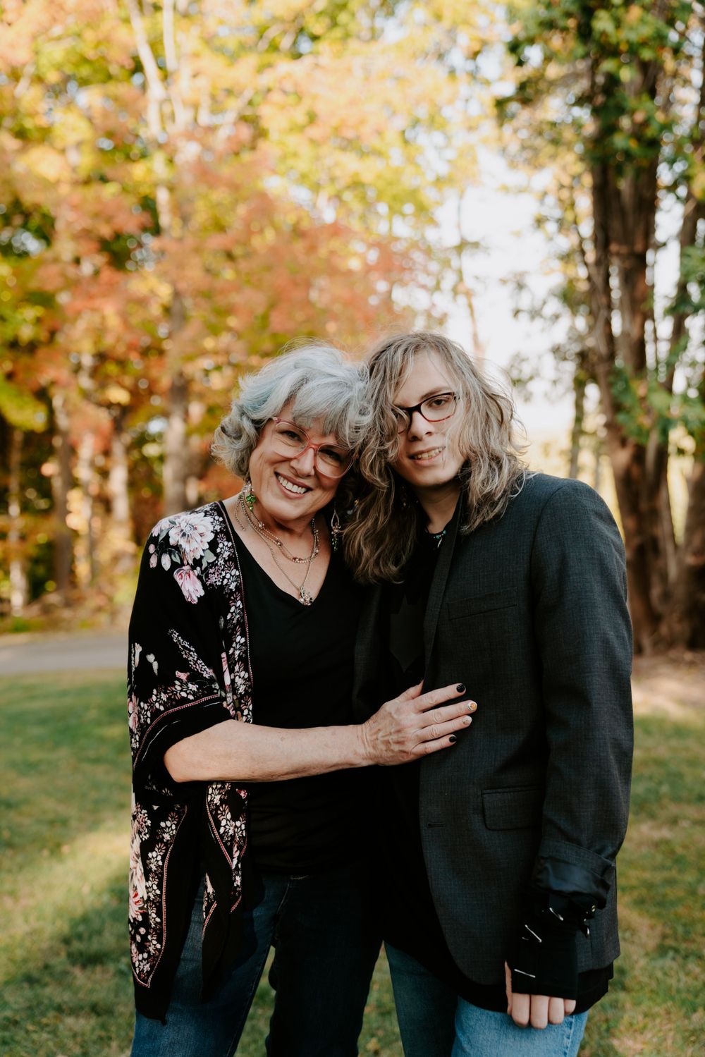 Three people embracing outdoors with autumn foliage in the background.
