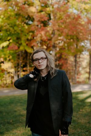 Person in dark clothing posing against vibrant fall trees.