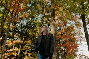 Person in dark clothing photographed against autumn foliage background.