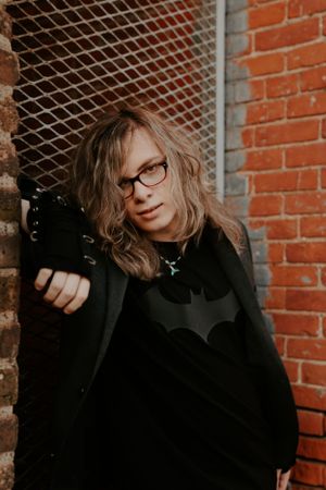 Person in dark clothing holding camera against brick wall background.