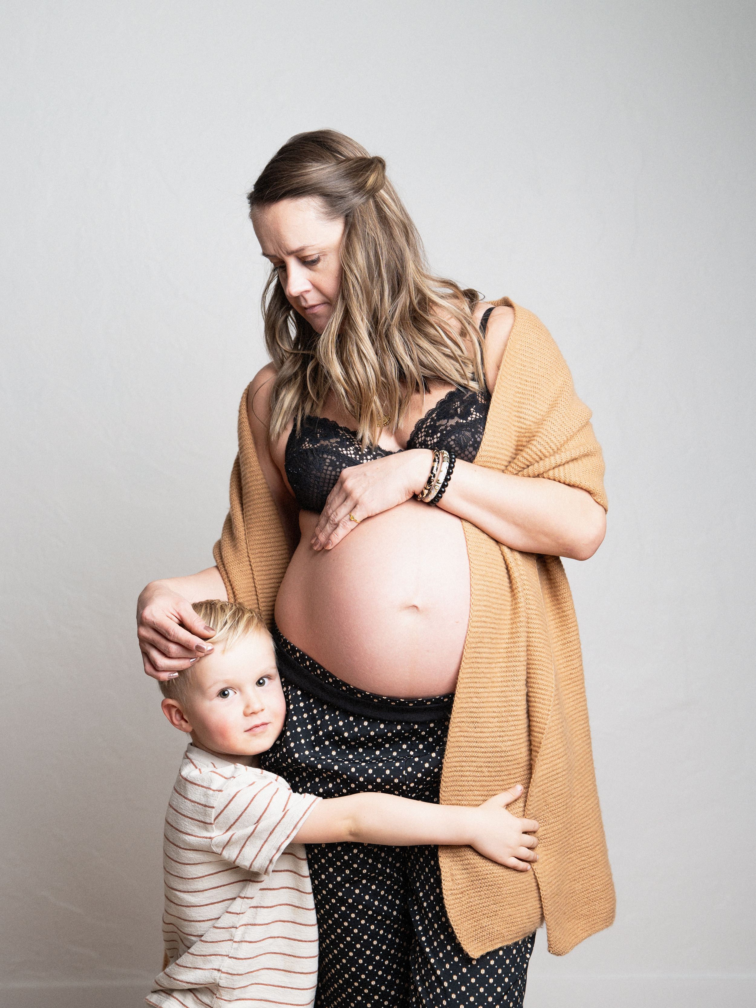 Intimate maternity portrait with loving embrace between figures against light gray background.