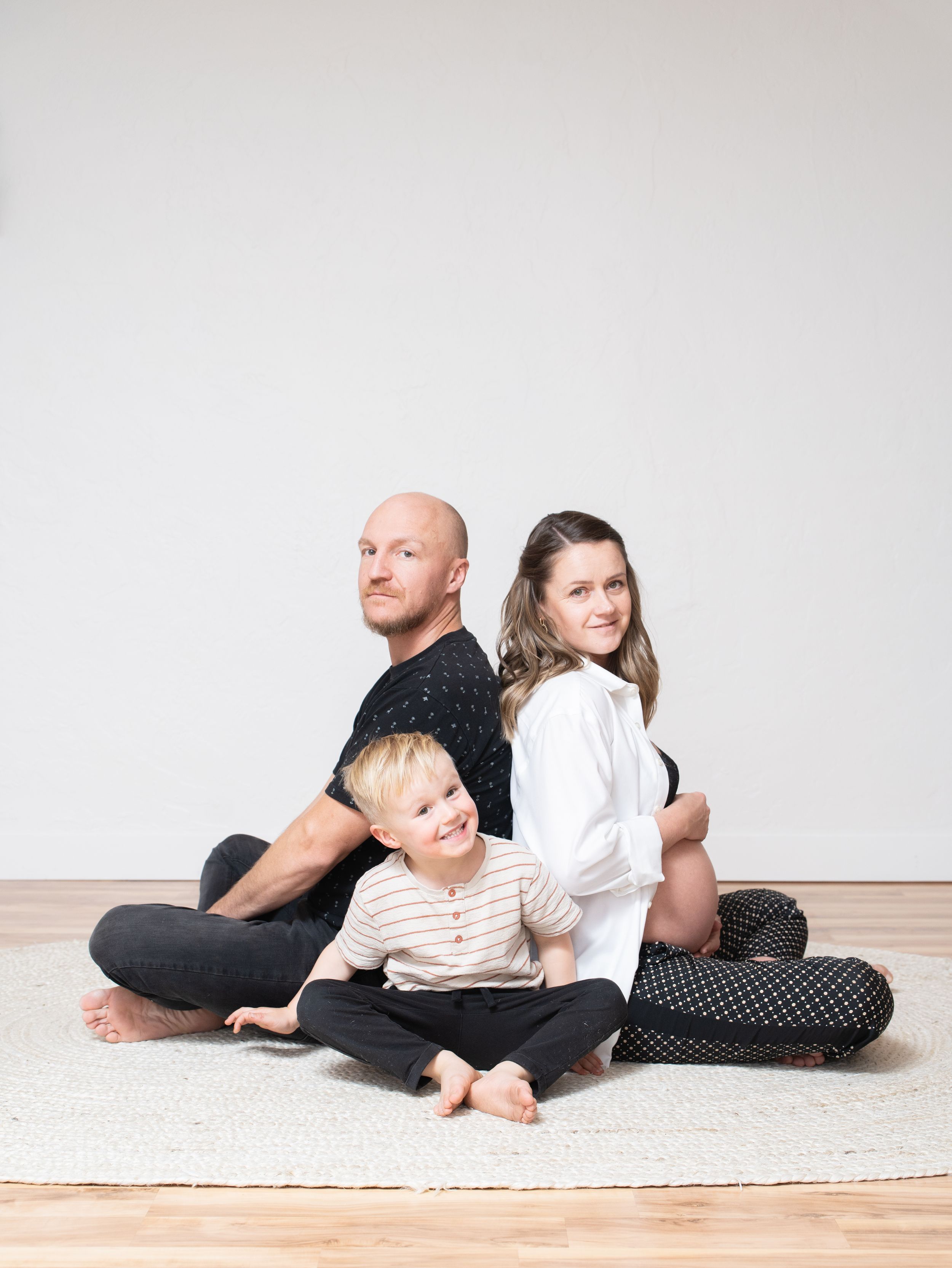 Family sitting together on floor with neutral background, showcasing casual intimacy and connection.