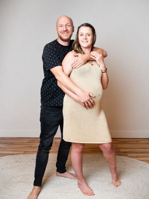 A couple poses together on a round rug, with one person in a beige dress and another in a black patterned shirt.