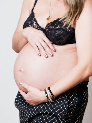 Close-up photo of a pregnant woman's belly in black lace lingerie showing a tender moment with hands on stomach.