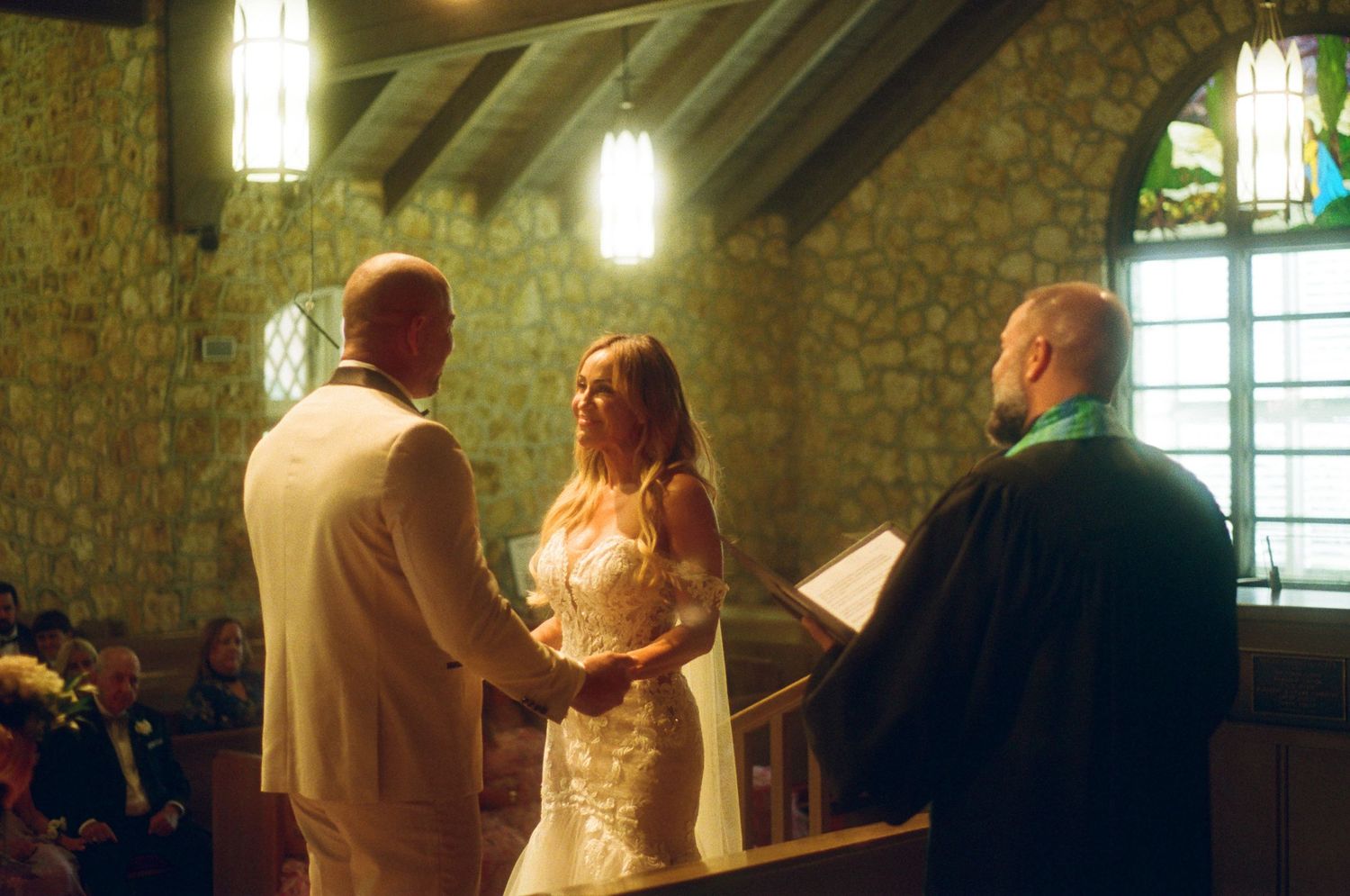 A wedding ceremony takes place inside a rustic stone chapel with glowing lantern lighting.