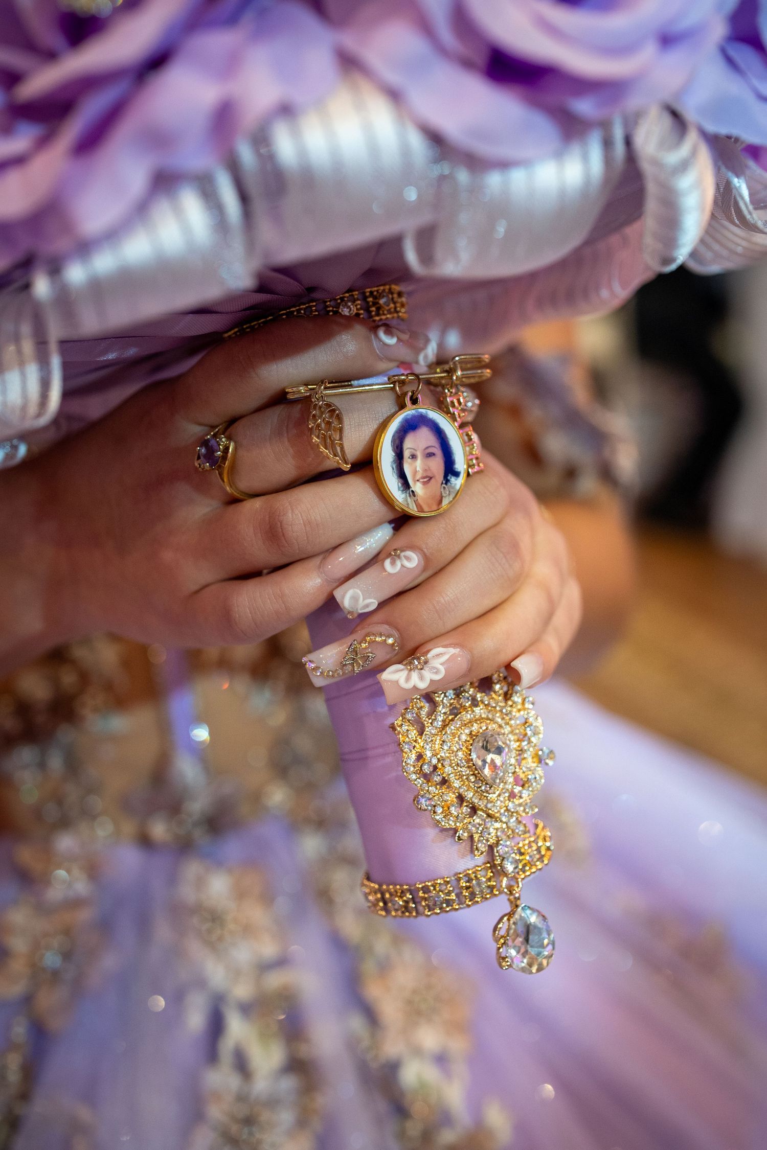 Close-up of decorated hands with rings and jewelry against purple fabric.