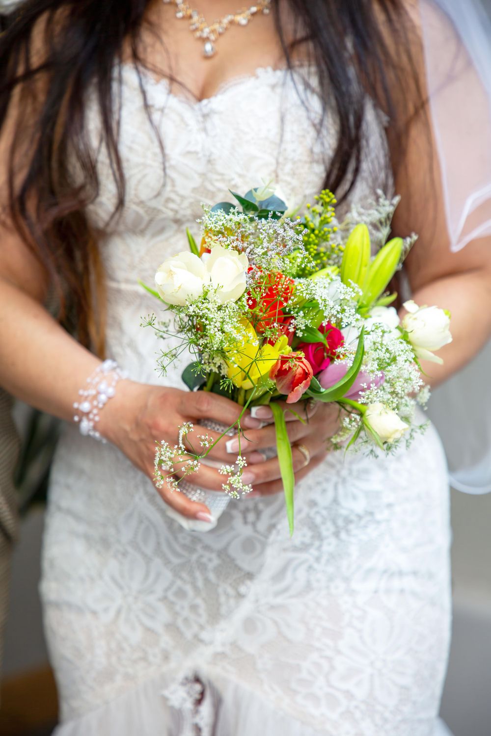 Close-up of bridal bouquet with colorful flowers and white lace dress details.