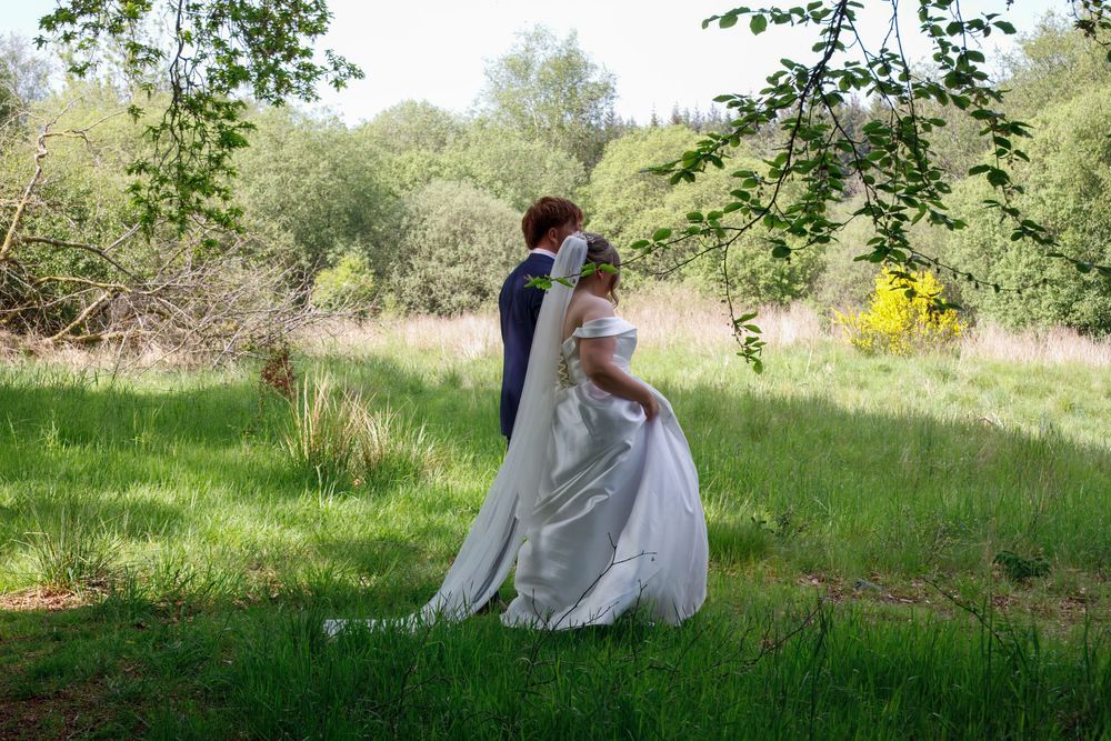 Bride and groom embracing in lush green meadow, bride wearing elegant white wedding dress.