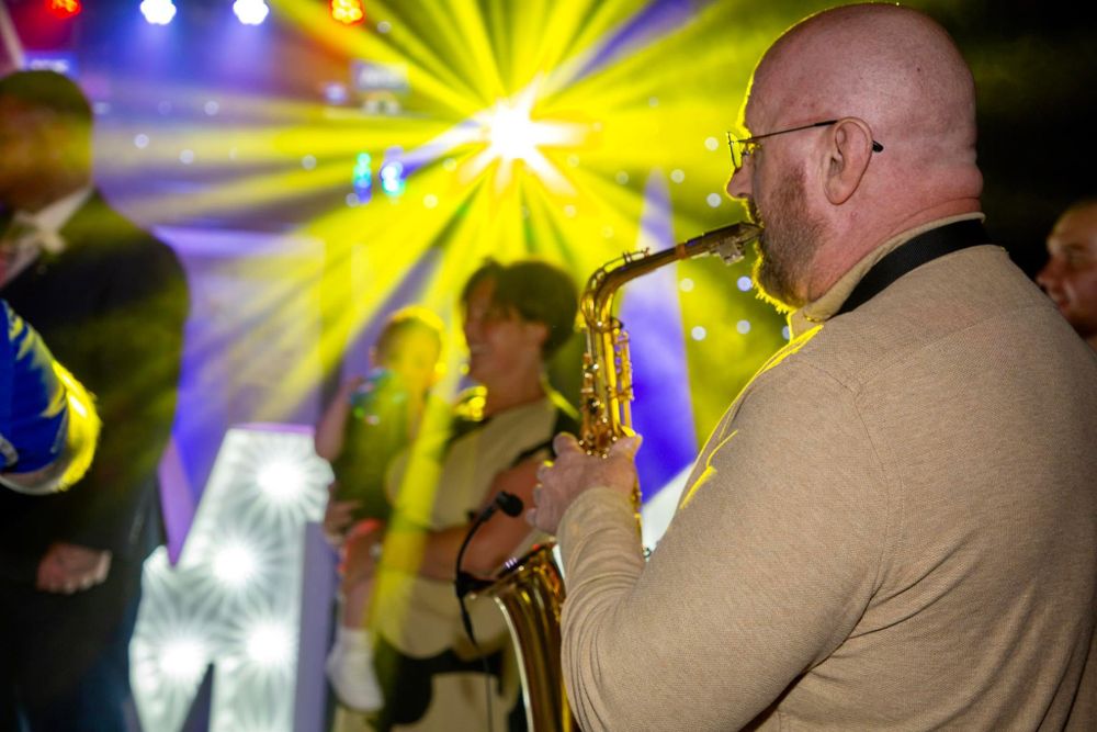 Saxophone player performs at a concert with colorful stage lighting in the background.