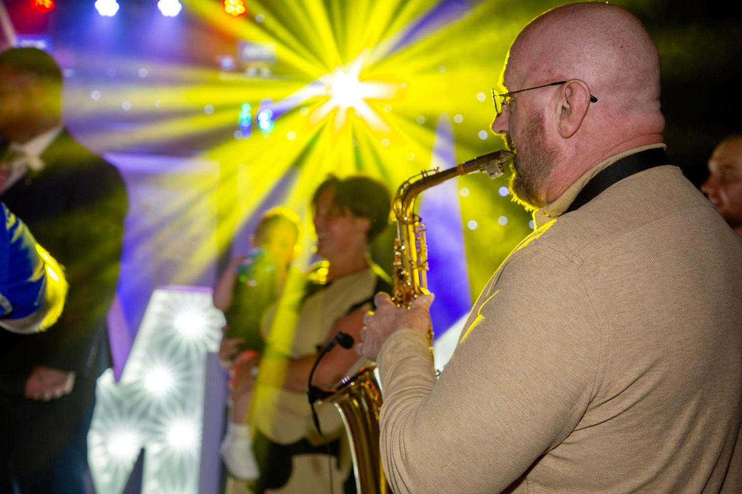 Saxophone player performs at a concert with colorful stage lighting in the background.