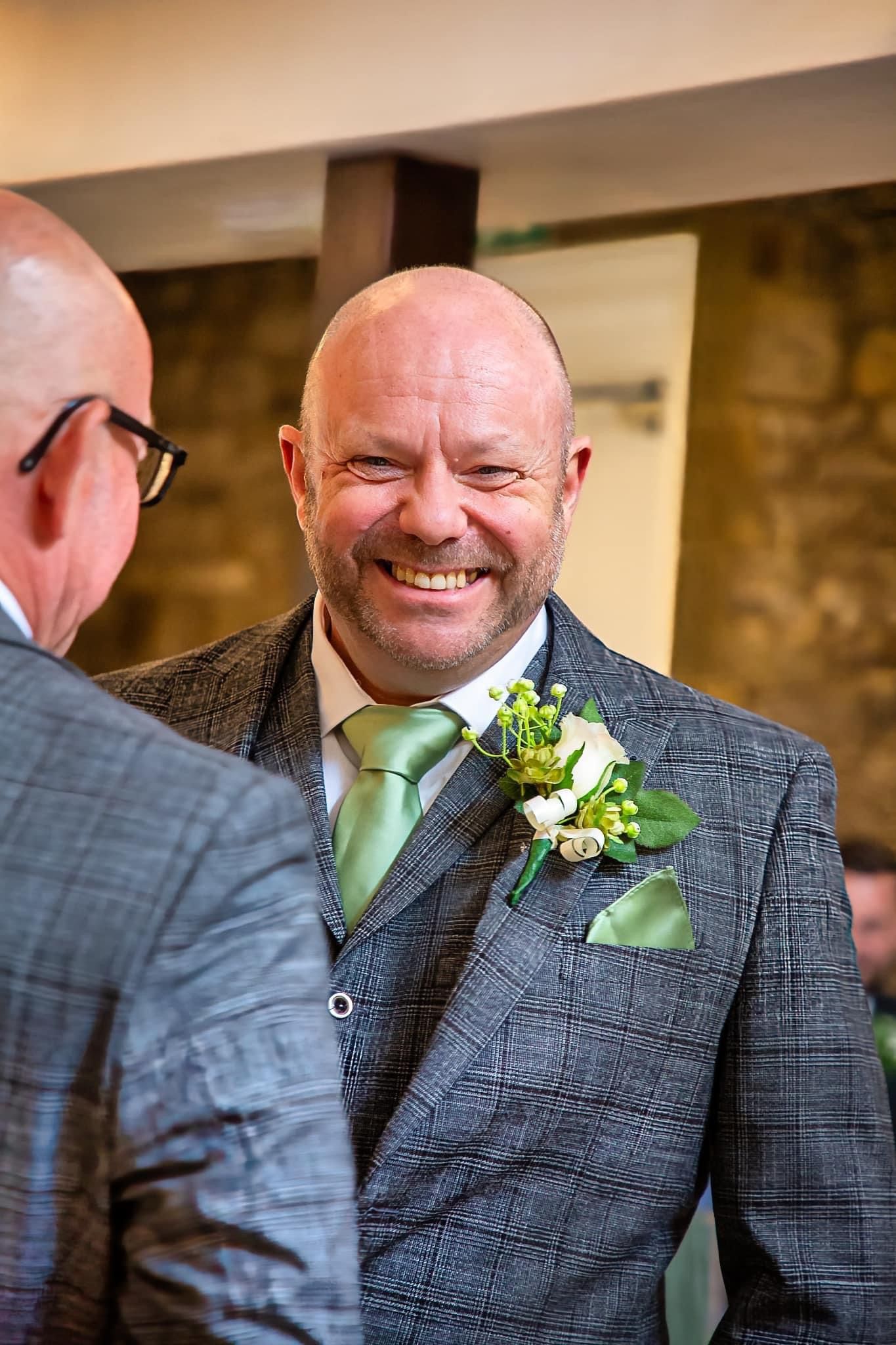 Wedding guest in grey suit and green tie wearing floral boutonniere.