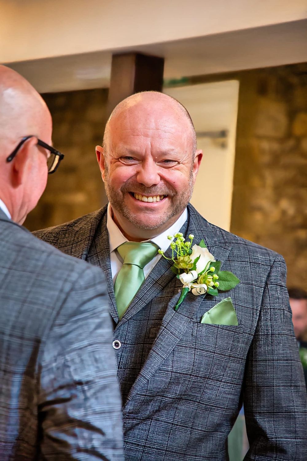 Wedding guest in grey suit and green tie wearing floral boutonniere.