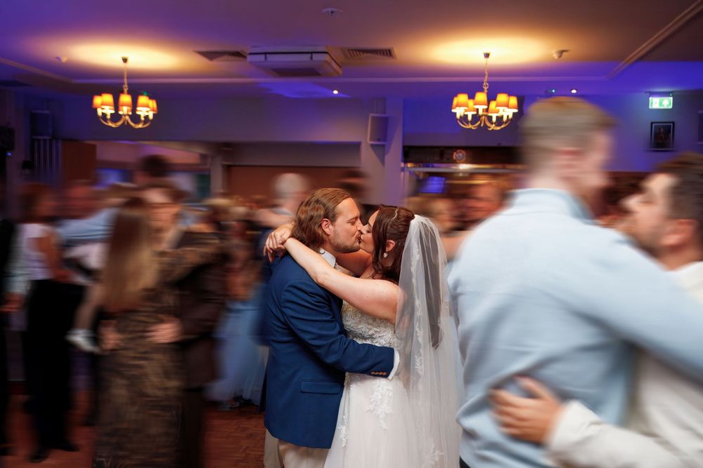 Bride and groom share first dance kiss surrounded by guests at wedding reception.