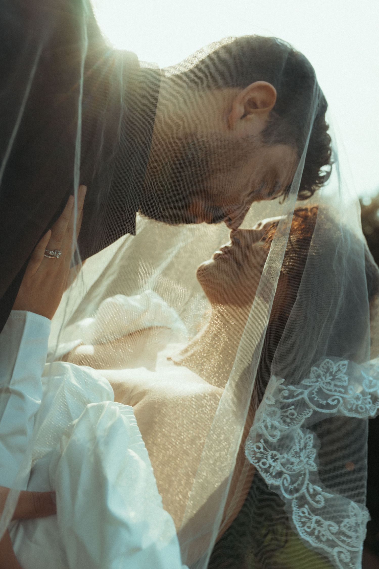 A romantic wedding moment captured in soft sunlight with delicate lace veil details.