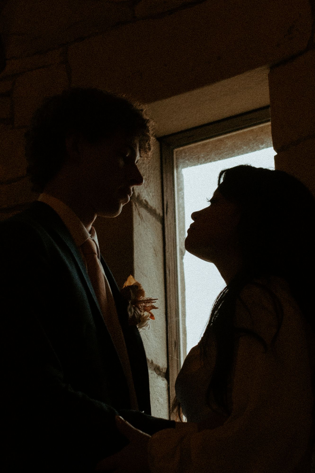 A romantic silhouette of a couple sharing an intimate moment by a window in moody lighting.