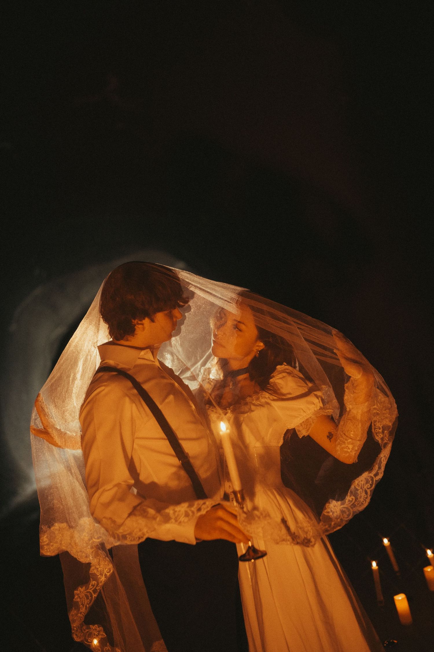 A romantic vintage-style scene of a couple in sepia tones under a lace veil with candlelight creating a warm glow.