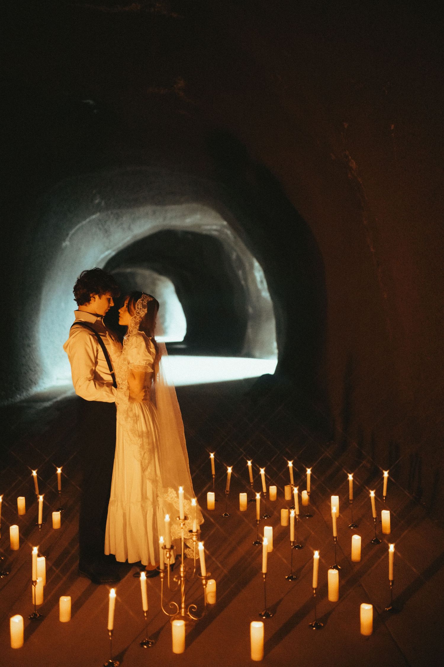 A romantic scene with two figures embracing in a tunnel surrounded by glowing candles arranged on the ground.