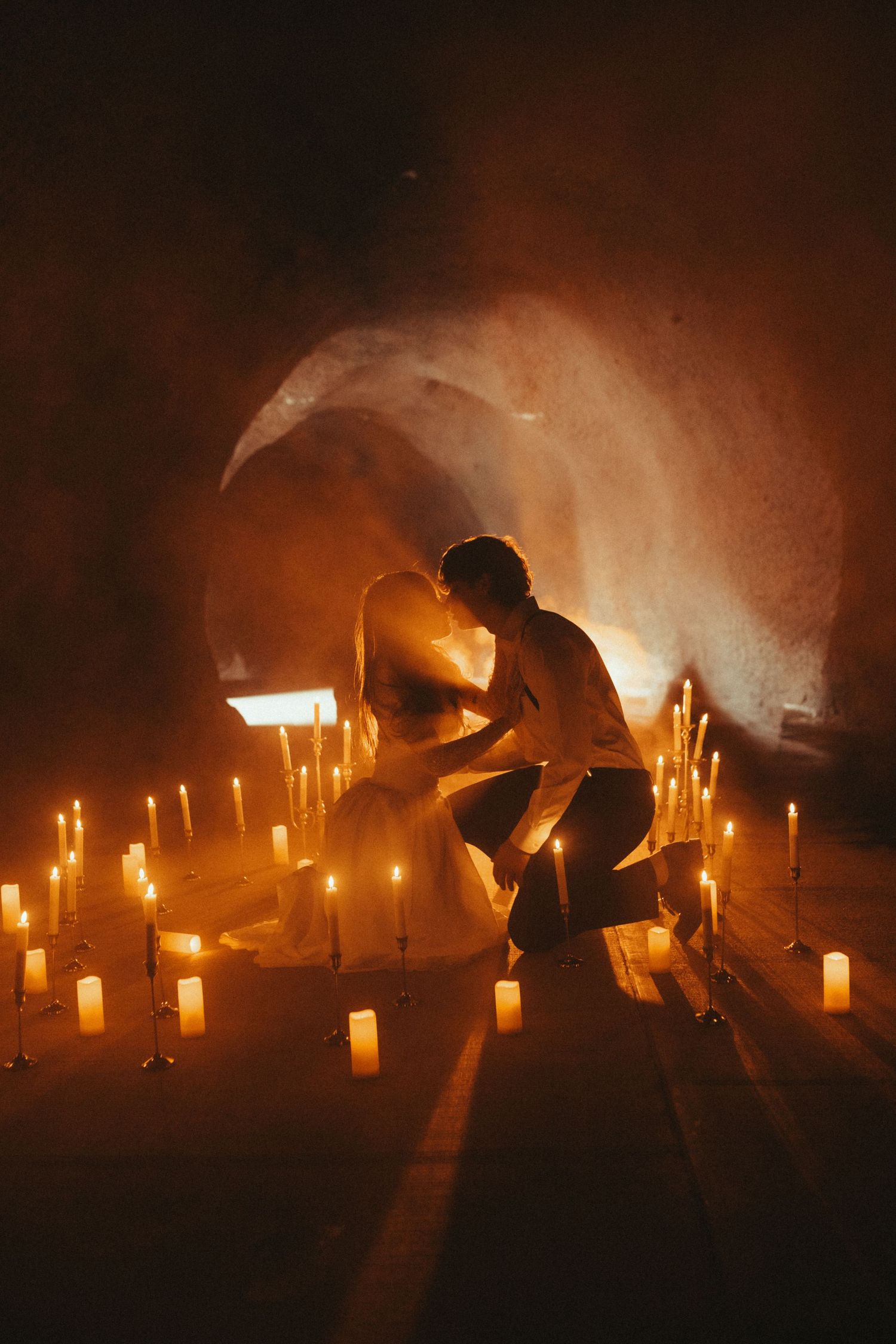 Silhouetted figures arrange glowing candles in a dark atmospheric setting creating a moody ceremonial ambiance.