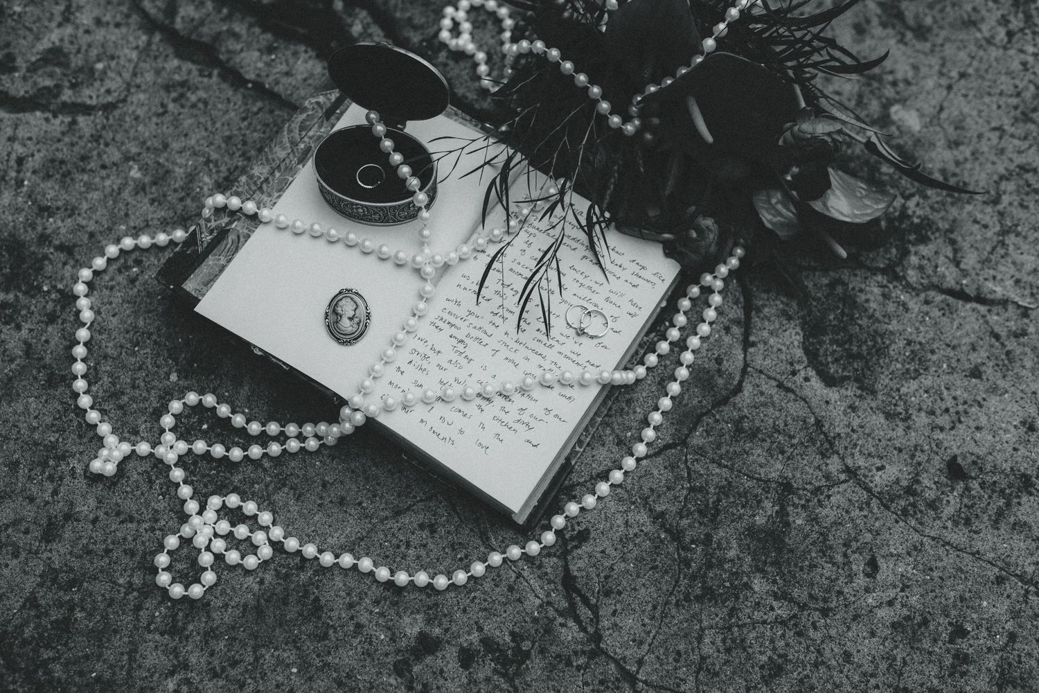 A vintage letter with black heart decoration and pearl necklace arranged on dark textured surface in monochrome.