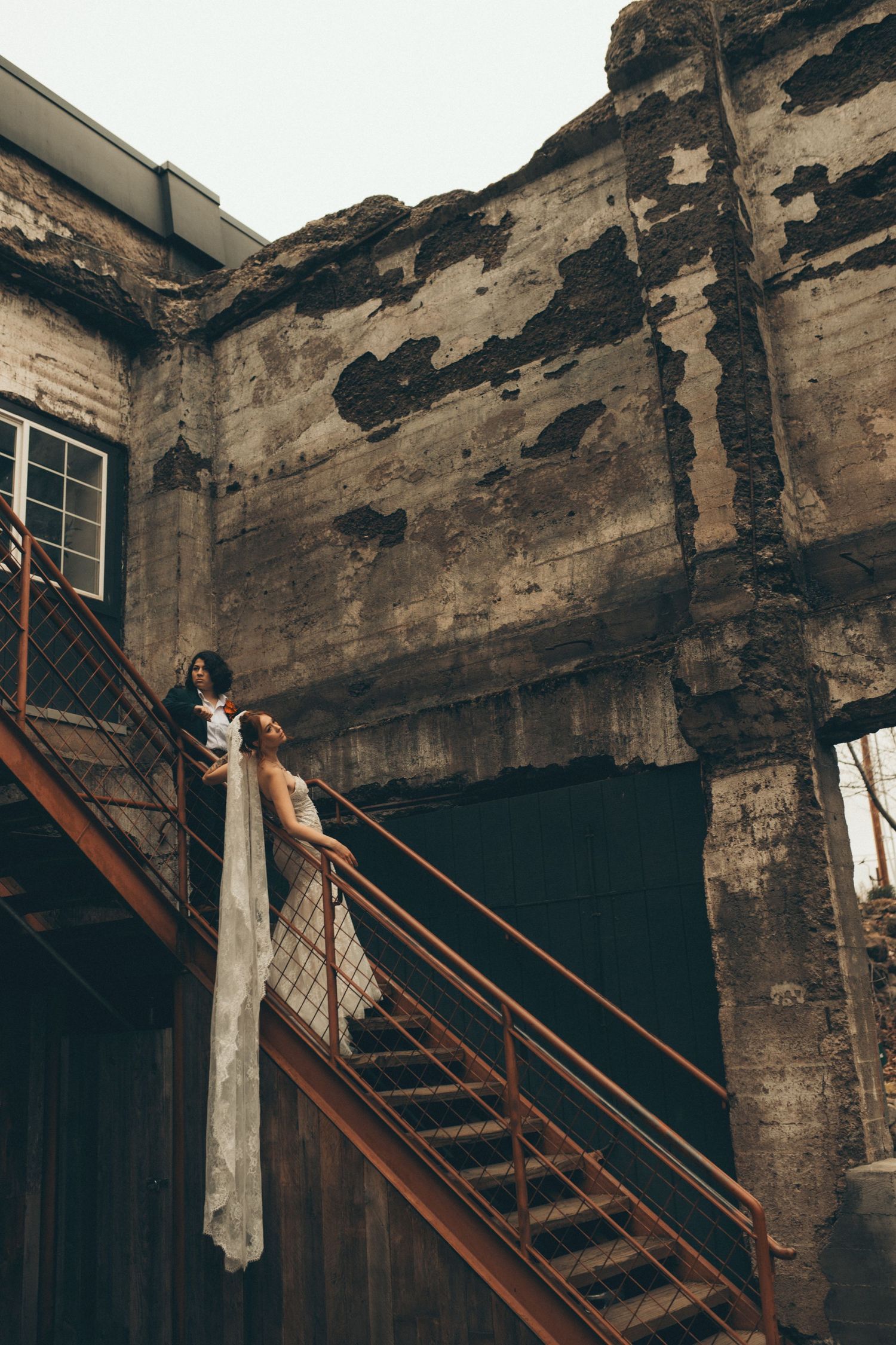 A dark and deteriorating interior staircase with exposed brick walls and wooden steps leads upward in an abandoned building.
