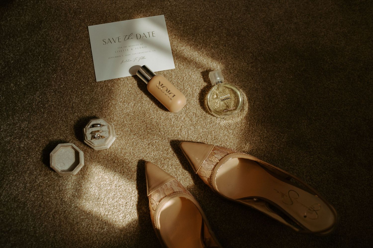 Wedding accessories including shoes, perfume bottle and invitation in dramatic lighting.