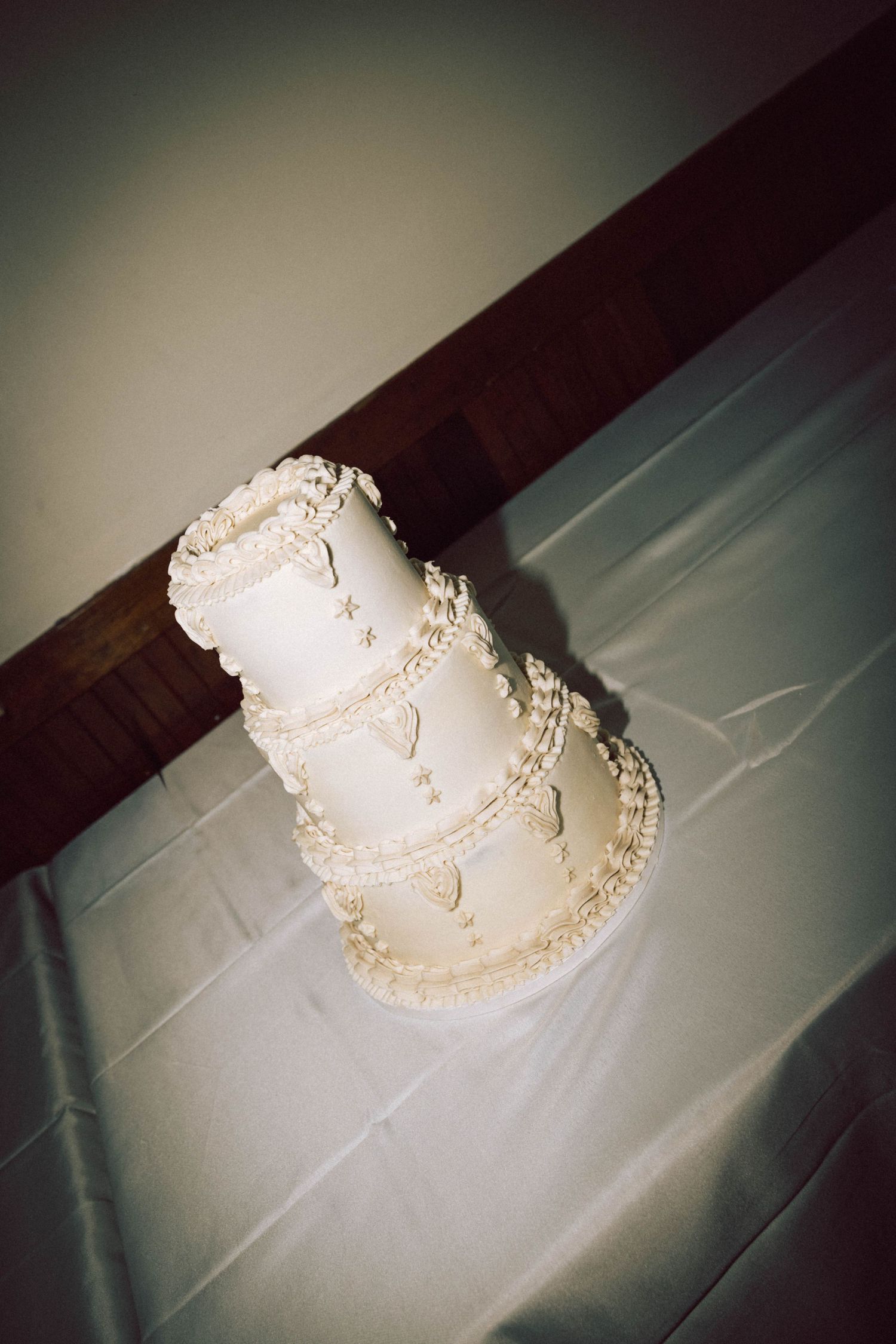Elegant three-tier white wedding cake with pearl and lace decorations on a white tablecloth.