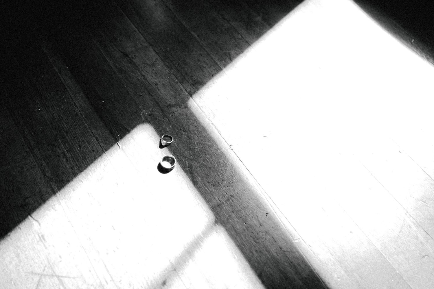 Black and white photo of two rings on a wooden floor with dramatic light and shadow contrast.