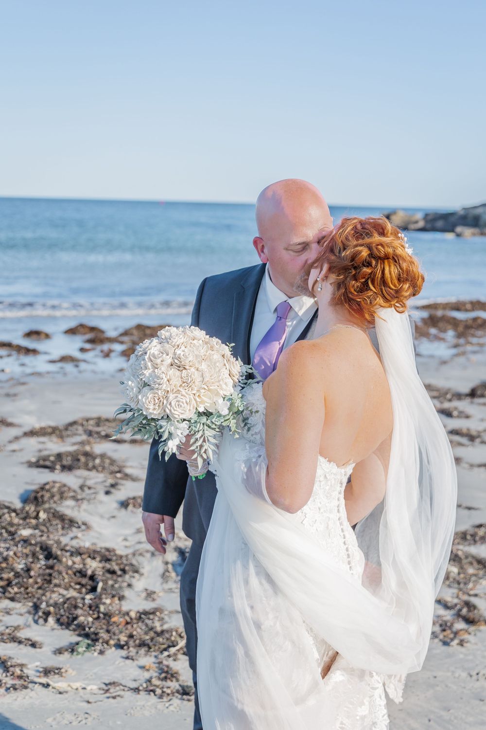A couple shares an intimate moment on a rocky beach during their coastal wedding.
