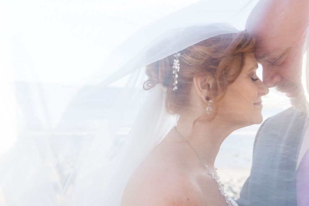 Ethereal wedding portrait through flowing white veil with soft dreamy lighting.