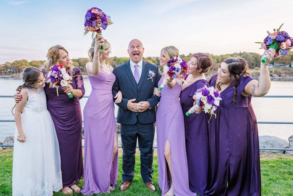 Bridesmaids in various shades of purple pose with groomsman in navy suit outdoors.