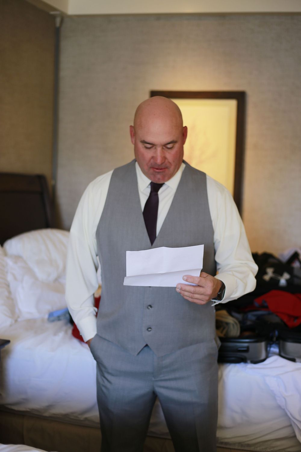 A person in formal attire reviews papers while standing in a hotel room before a wedding ceremony.