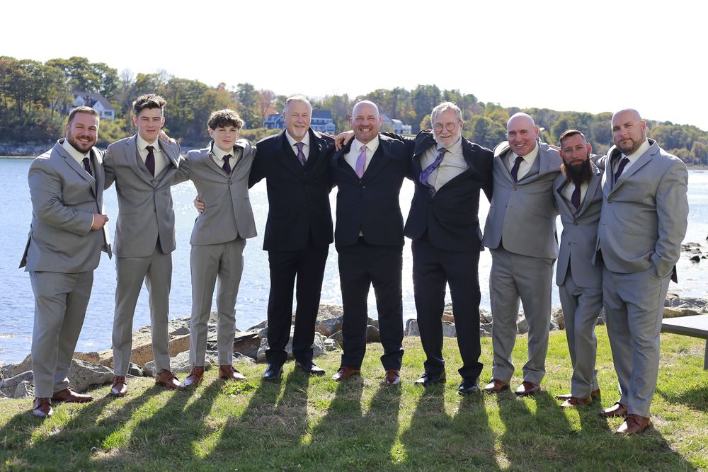 Wedding party poses together on waterfront wearing coordinated gray suits.