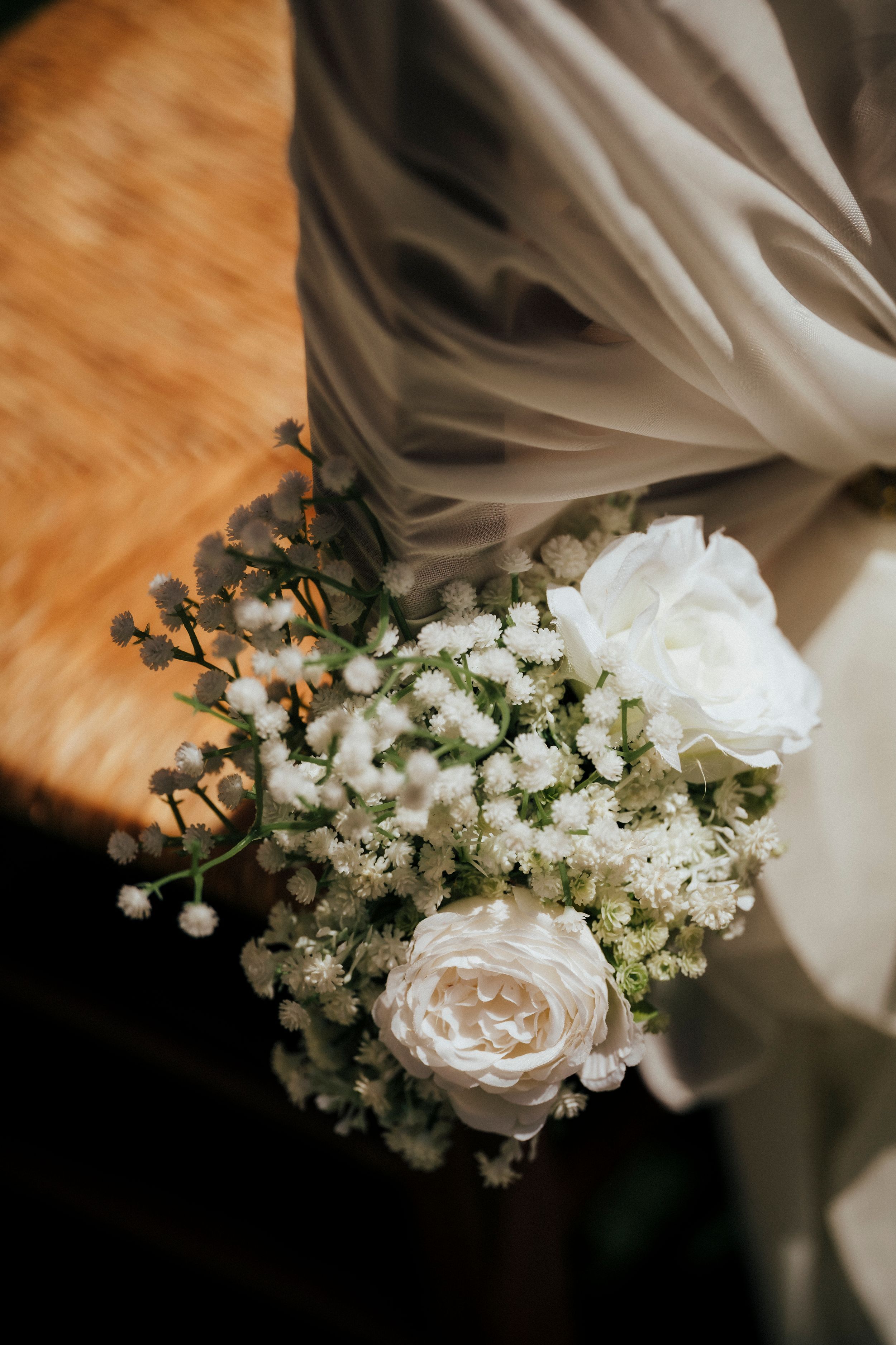 Delicate white rose and baby's breath bouquet arrangement on wooden surface.