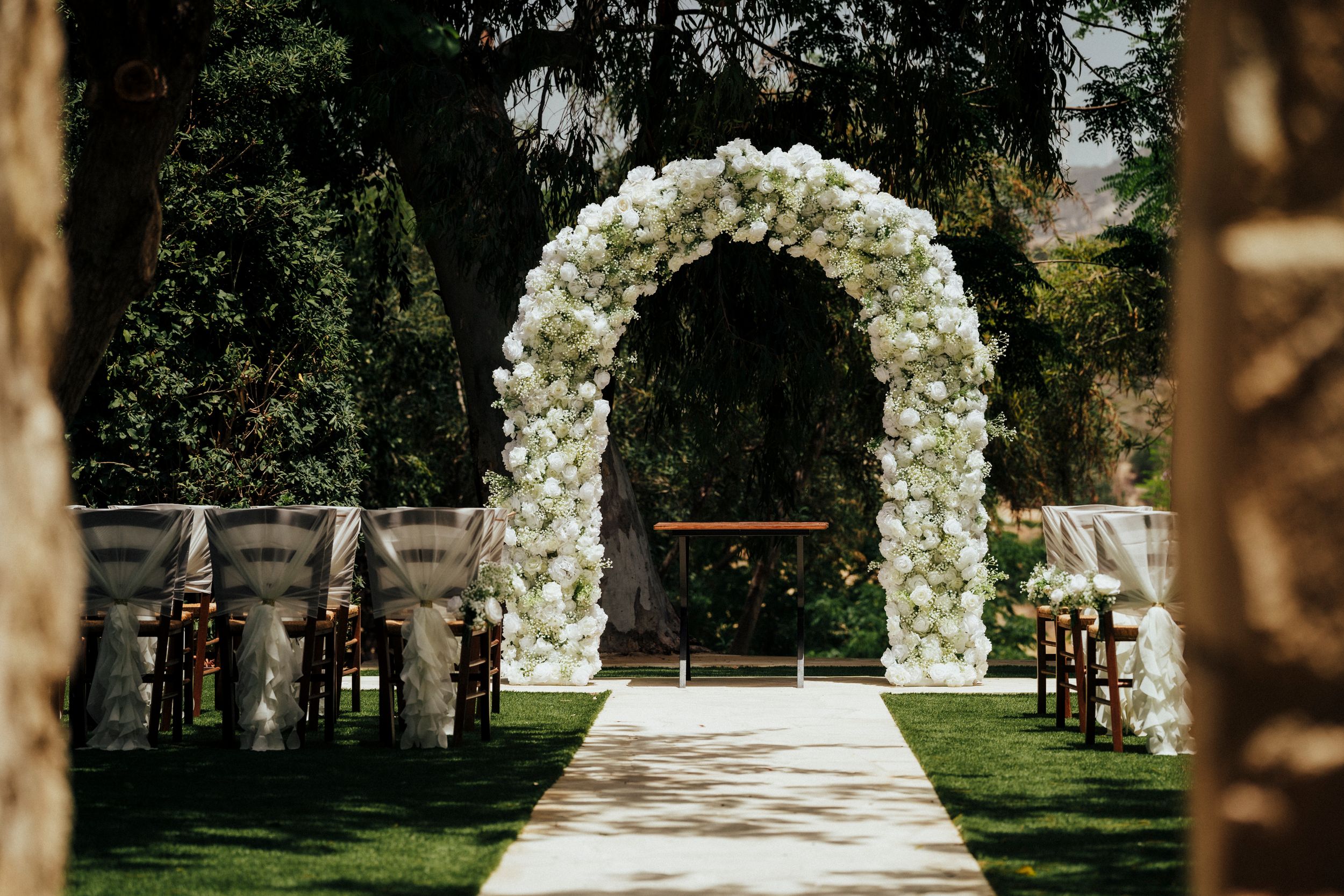 Elegant white floral arch frames outdoor wedding ceremony space with stone pathway.