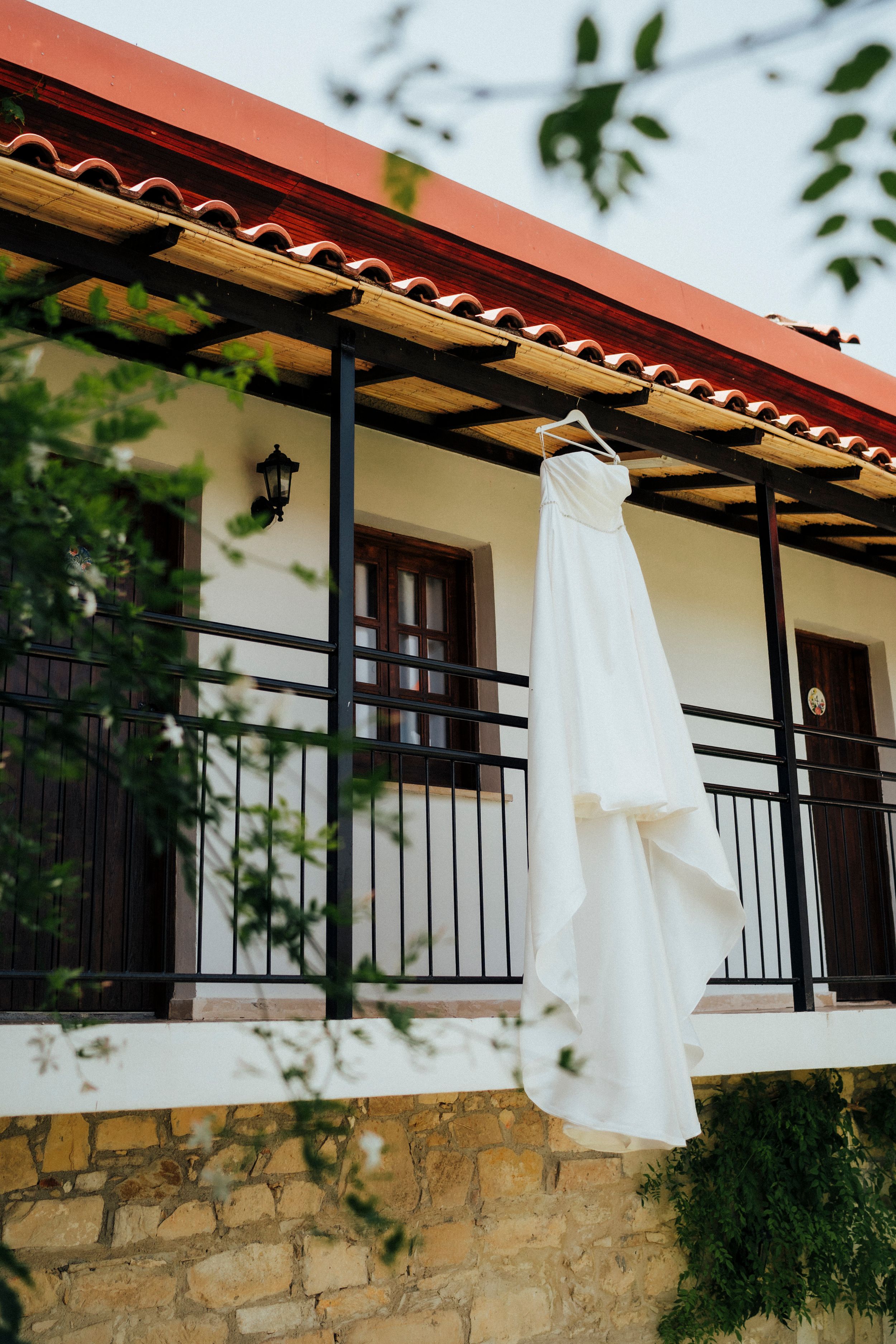 White wedding dress hanging on balcony of Mediterranean-style building with terra cotta roof.