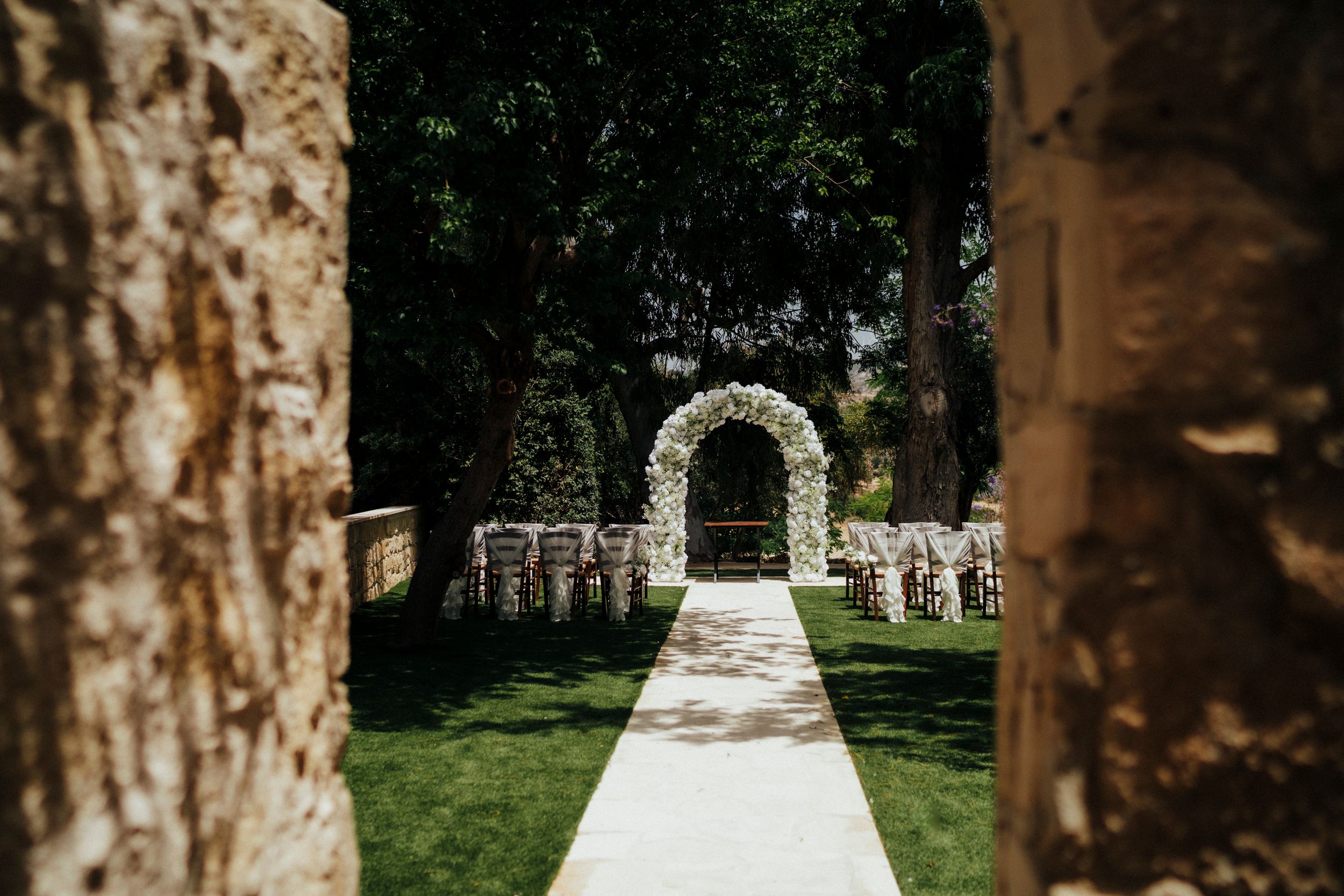 White floral arch at the end of a stone pathway leads to an elegant outdoor wedding ceremony setup.