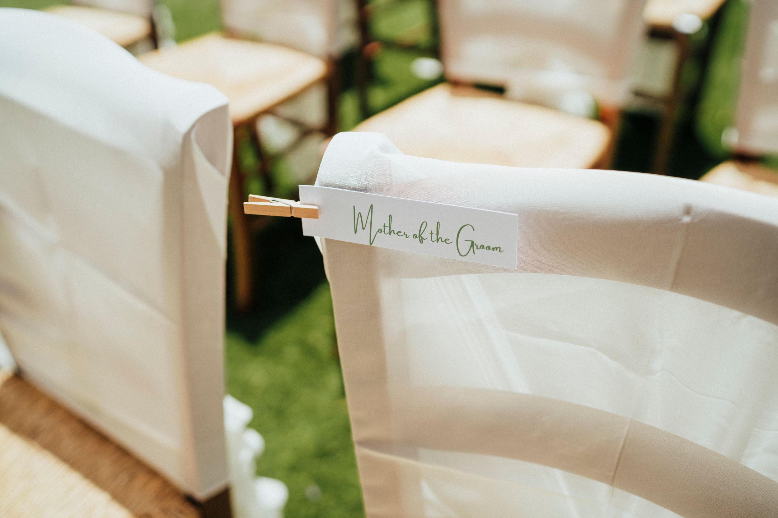 Close-up of elegant white chair cover with name card attached at outdoor wedding venue.