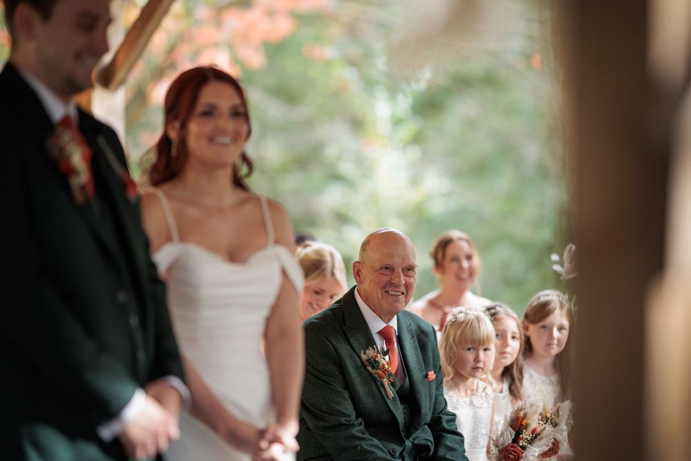 Wedding ceremony guests seated outdoors under trees with natural lighting creating a romantic atmosphere.