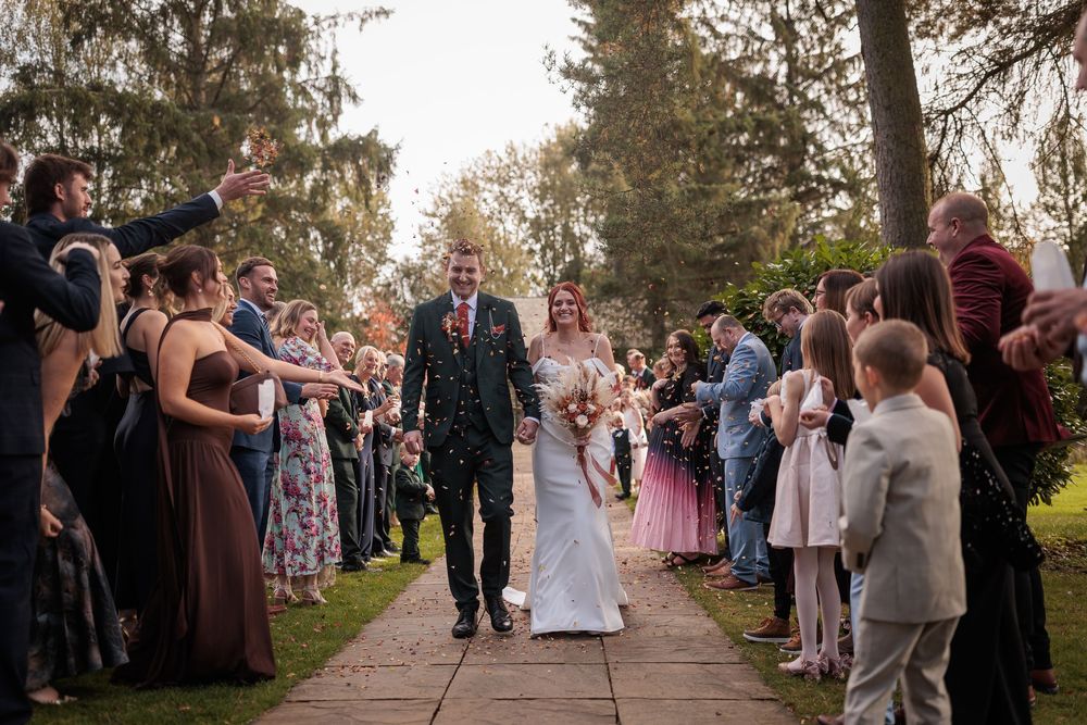 Wedding guests line up outdoors to create a bubble-filled exit pathway for the newlyweds at a garden ceremony.