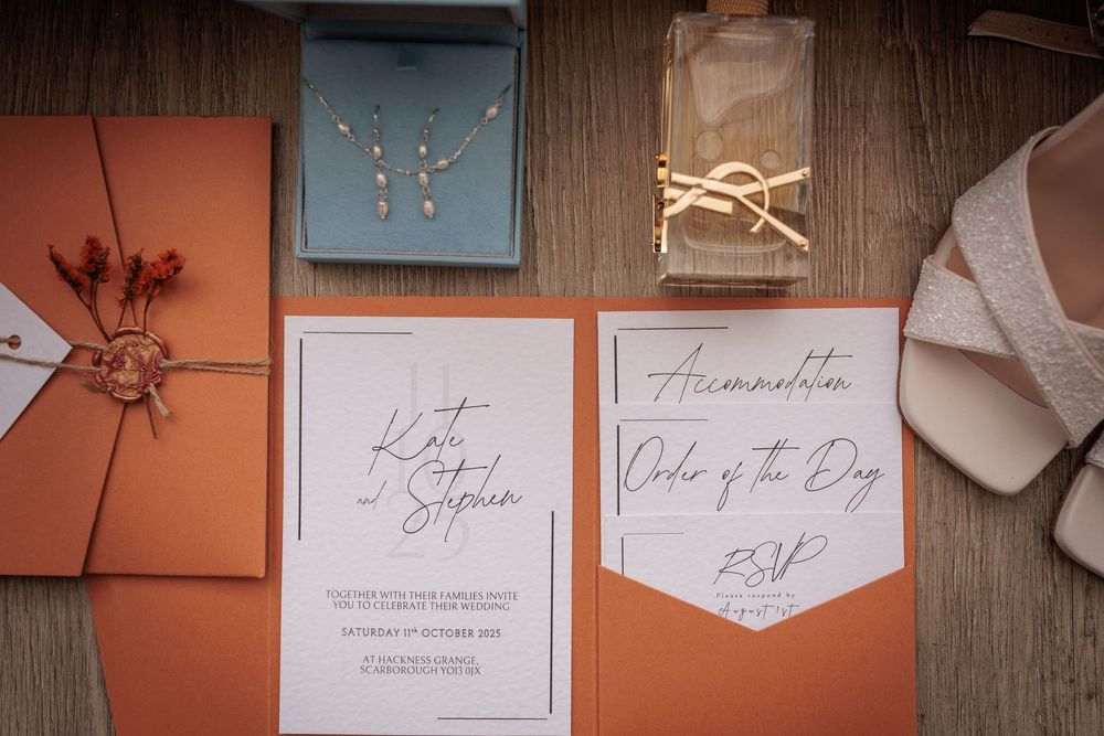 Elegant wedding invitation suite with coral and white stationery pieces laid out on a rustic wooden surface.