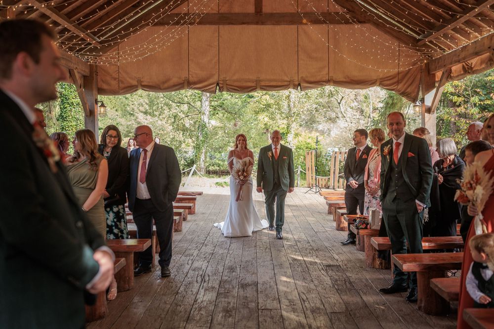 Rustic wooden barn interior decorated with string lights for wedding ceremony with guests seated on benches.
