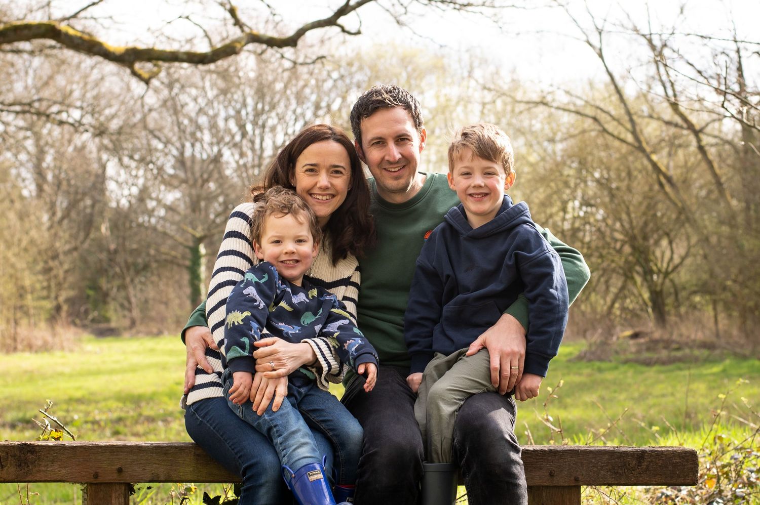 Family of 4 sitting on a bench during a family autumn photoshoot, all looking at the camera