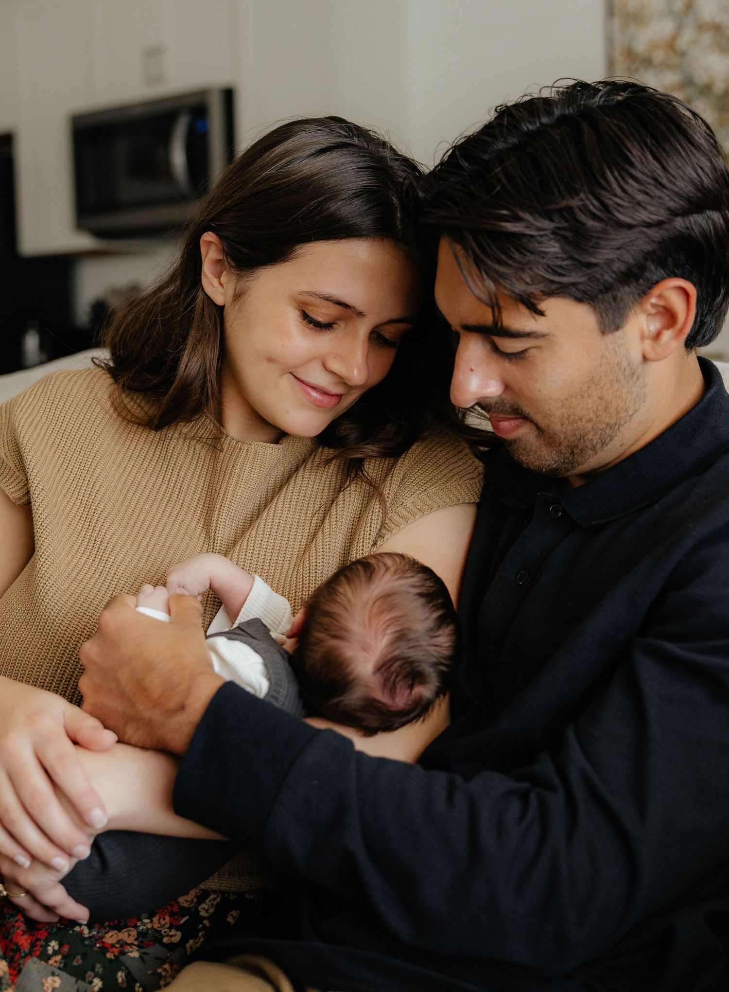 New parents tenderly cradling their sleeping newborn baby together on a cozy couch at home.