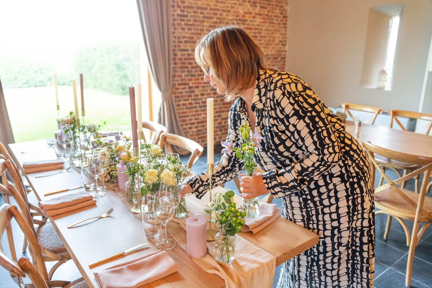 Event decorator arranging table settings in rustic brick-walled dining space.